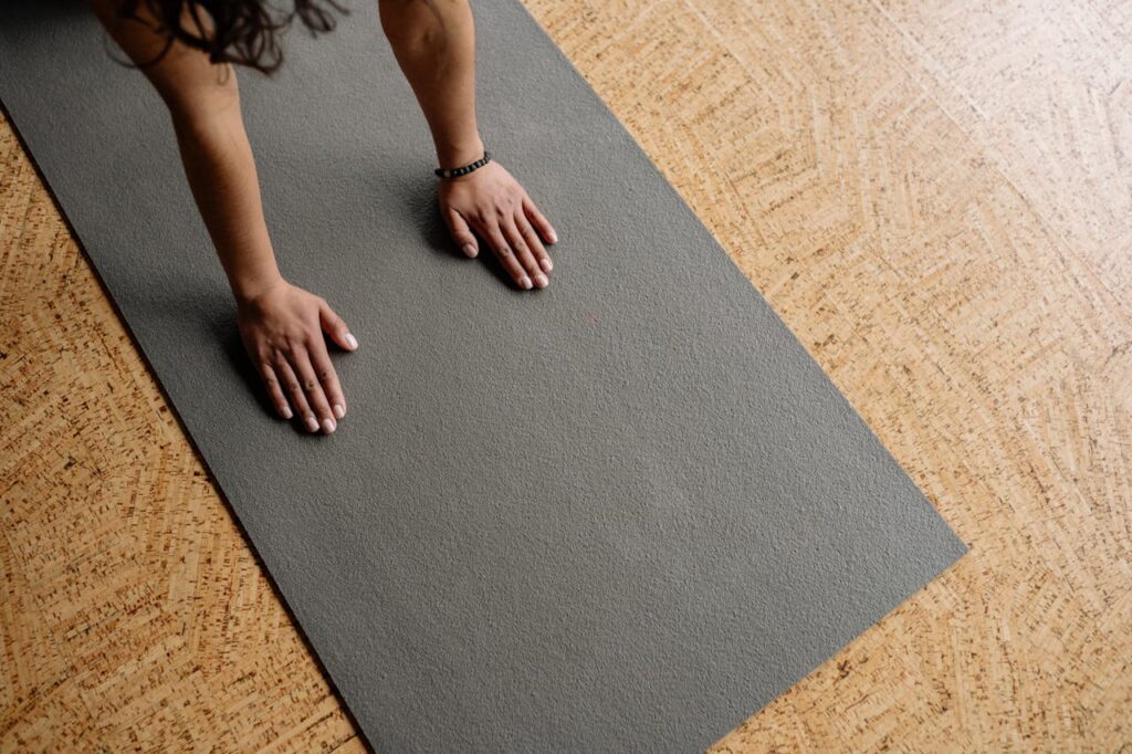 Hands placed on a gray yoga mat on a cork floor.