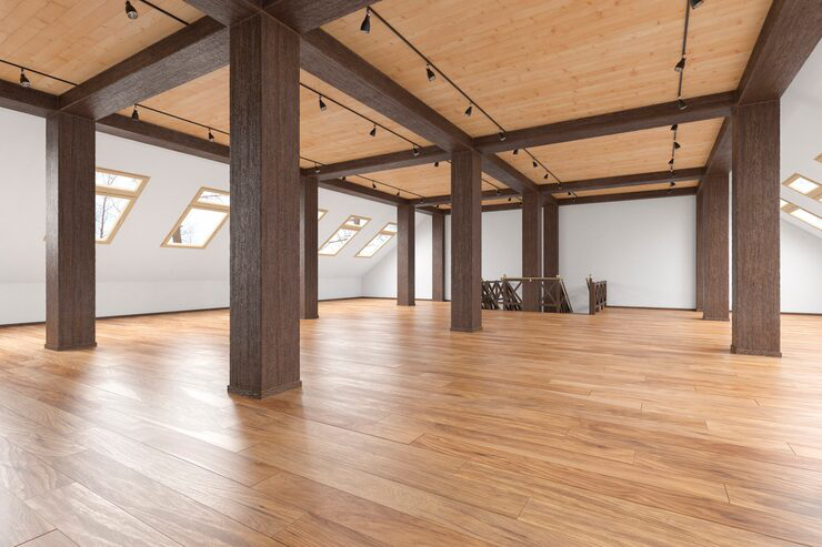 Open loft-style interior with wooden beams, sloped ceilings, and wide plank wood flooring in a bright empty space.