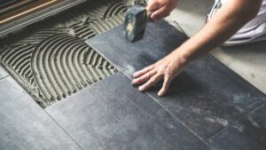 A person installing large, dark grey floor tiles