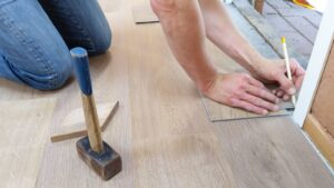 A craftsman carefully measuring and marking wooden floor panels for precise flooring installation.