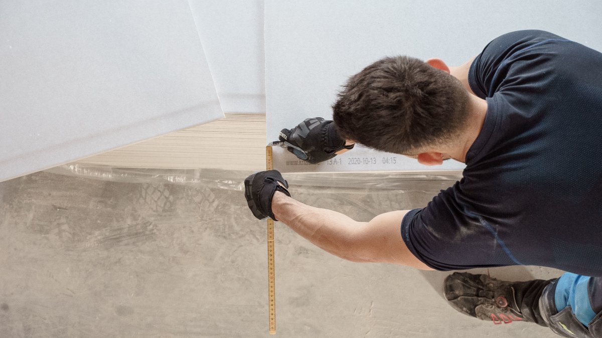 Construction worker measuring and cutting flooring panels during flooring preparation.